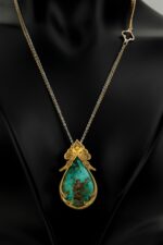 A necklace on a dress made of brass metal with gold plating and Shajar Neyshabur turquoise stone and using the art of penmanship in its design.